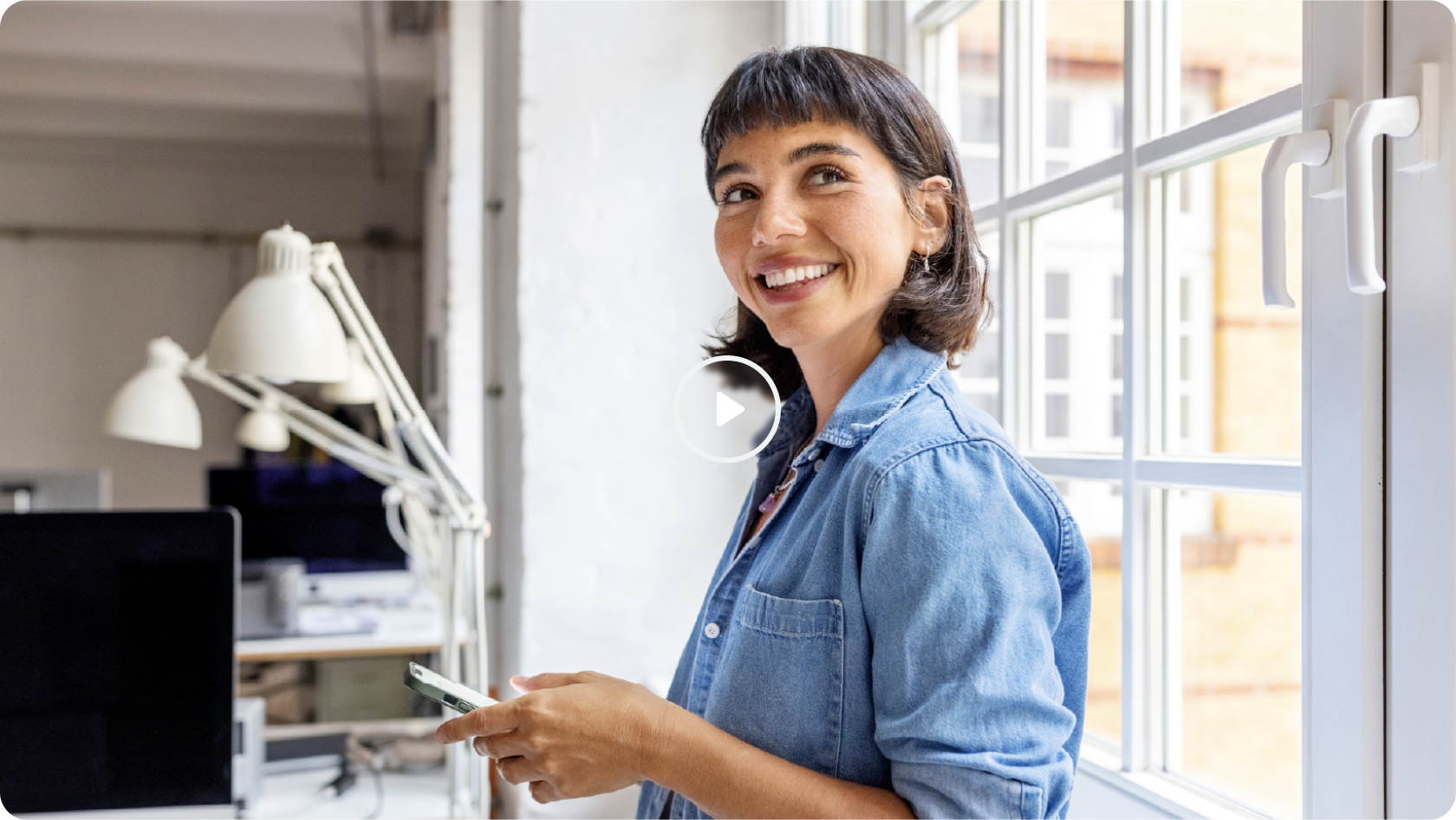 A woman at work place holding phone in her hand with a smile