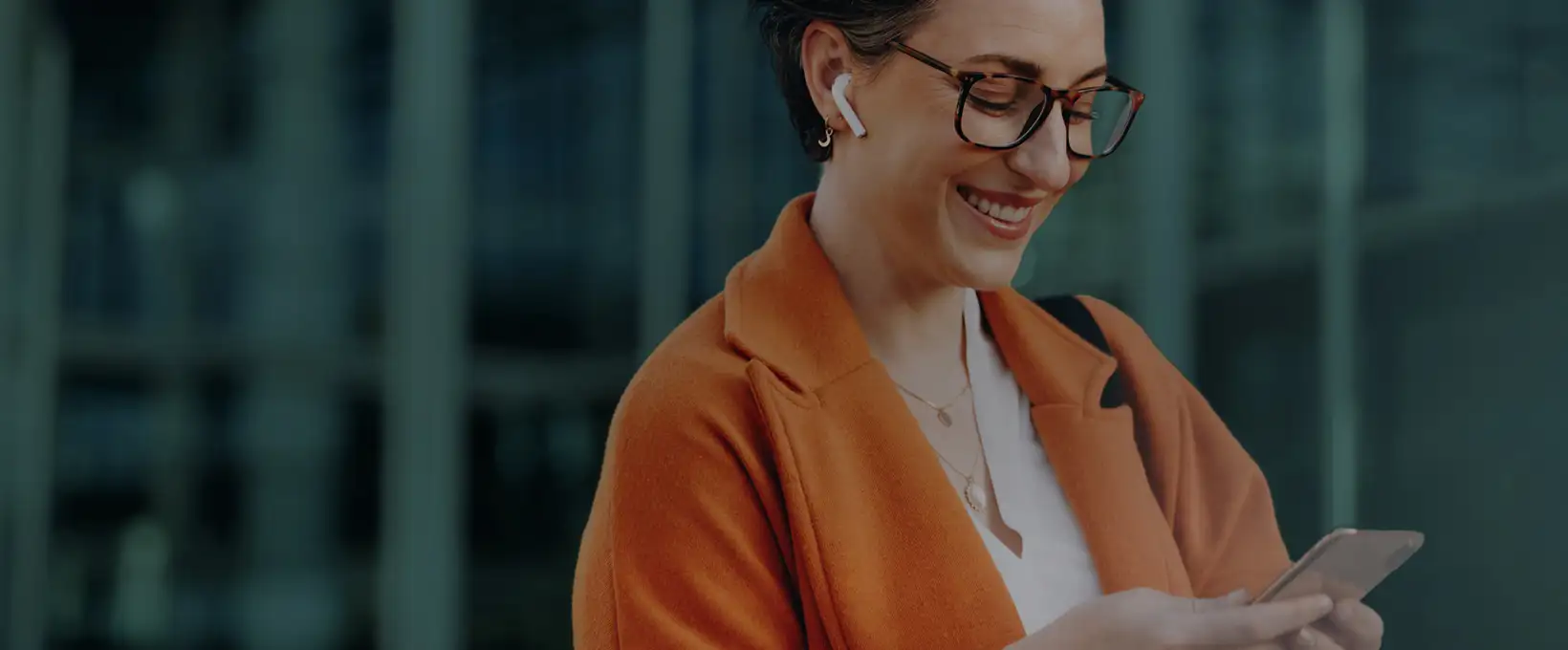 Woman in an orange jacket smiling while looking at her phone