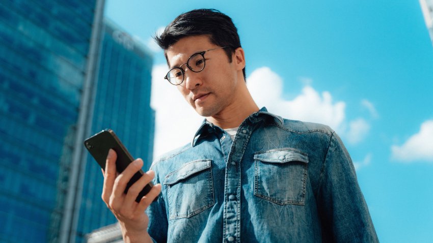 A gentleman in denim shirt looking at phone screen and the view of Highrise buildings in the background
