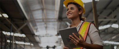 Woman working in a construction area wearing a hardhat and carrying a tablet