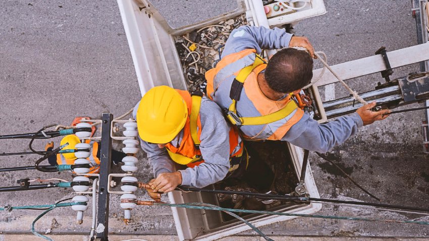 Two electricians with safety equipment are working to install electrical power lines 