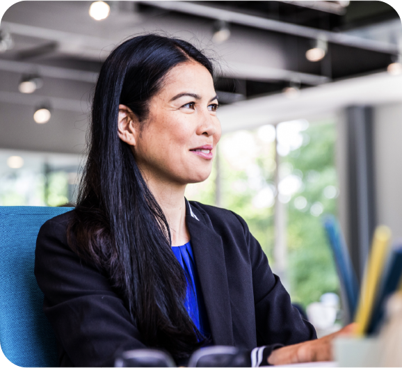 A smiling woman in a black suit sitting at her office desk