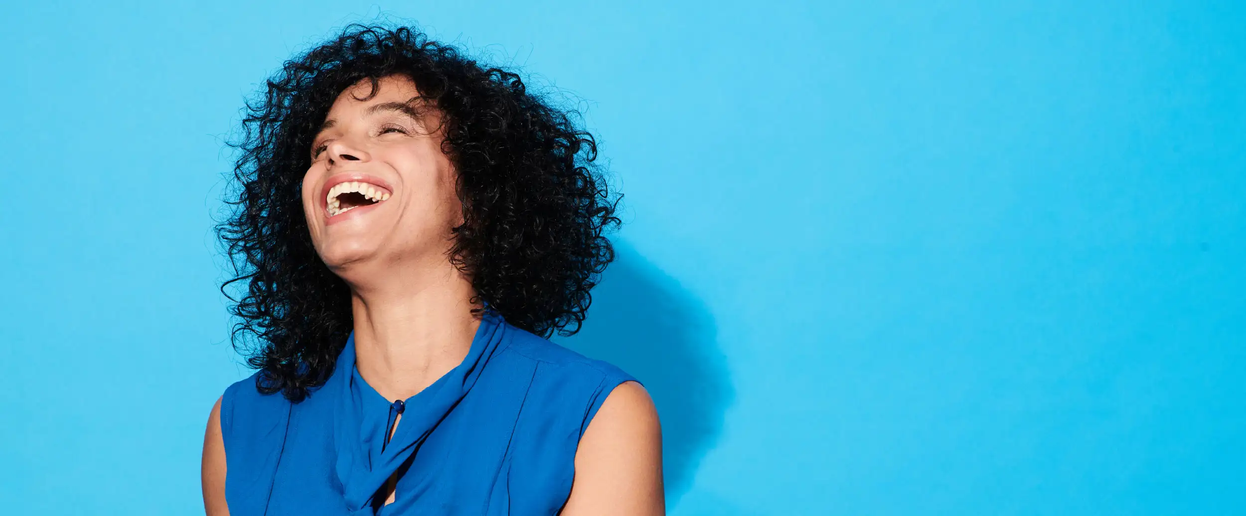 Woman dressed casually laughing in front of a blue background