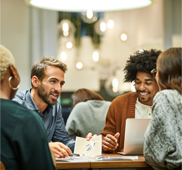 A group of four people sitting at a table with a laptop having a business meeting