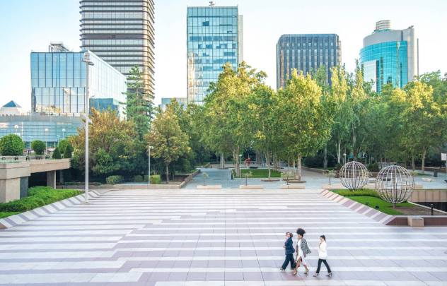 Three women walking along an urban square and skyscrapers in background