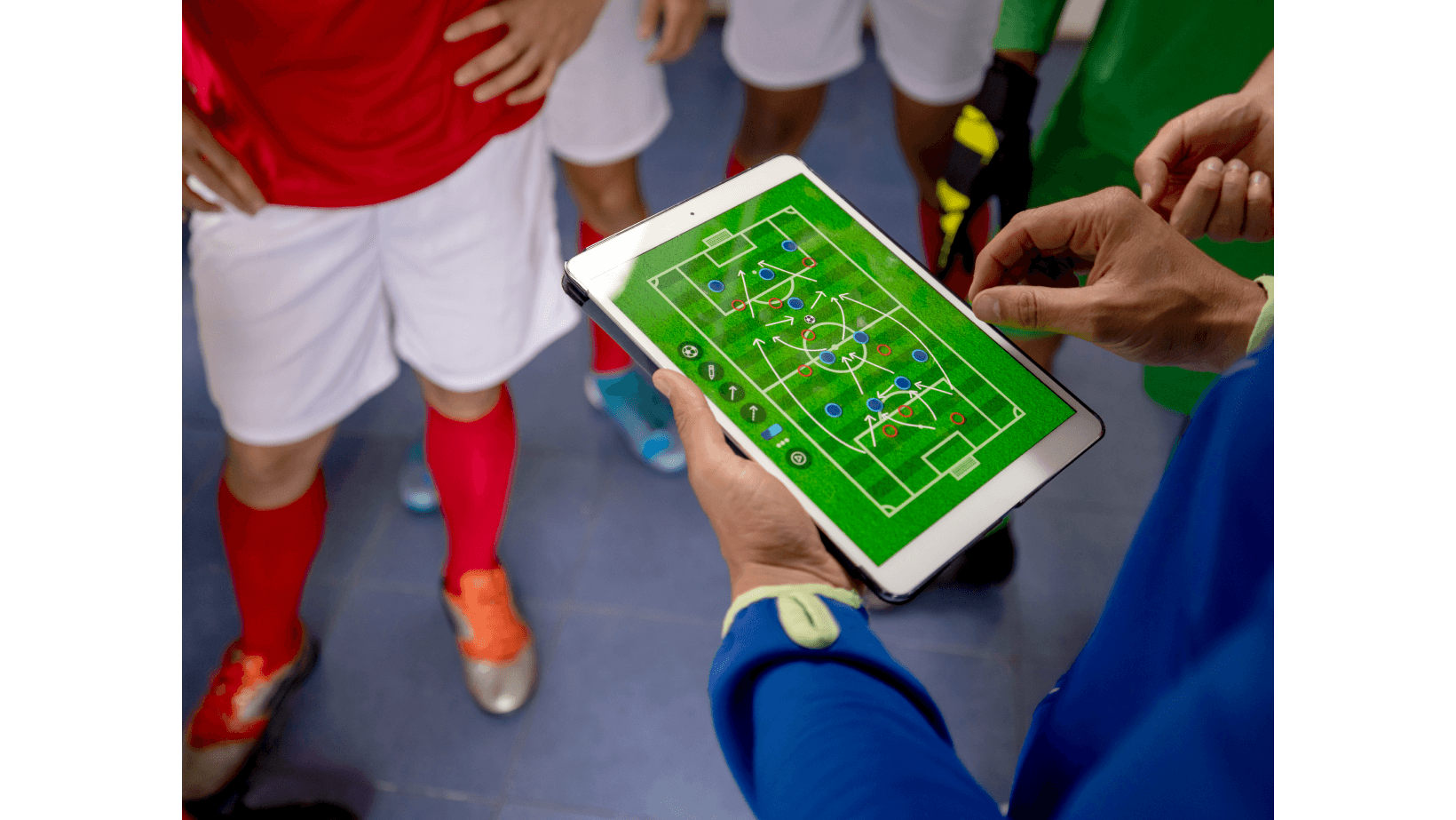 A Soccer coach reviewing game tactics plan on tablet with the team in the dressing room