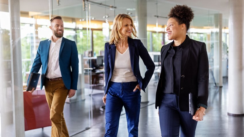 Three young professionals in formal dress walking through the office corridor with the smile on their faces