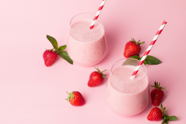Two pink yogurt smoothies with strawberries on a pink background