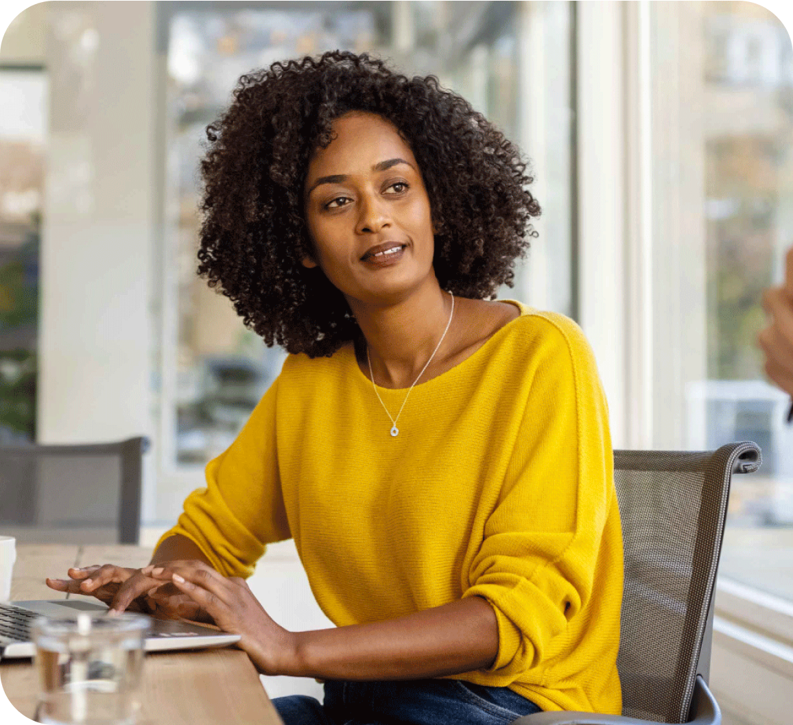 A picture of woman in yellow top looking at the side while using laptop