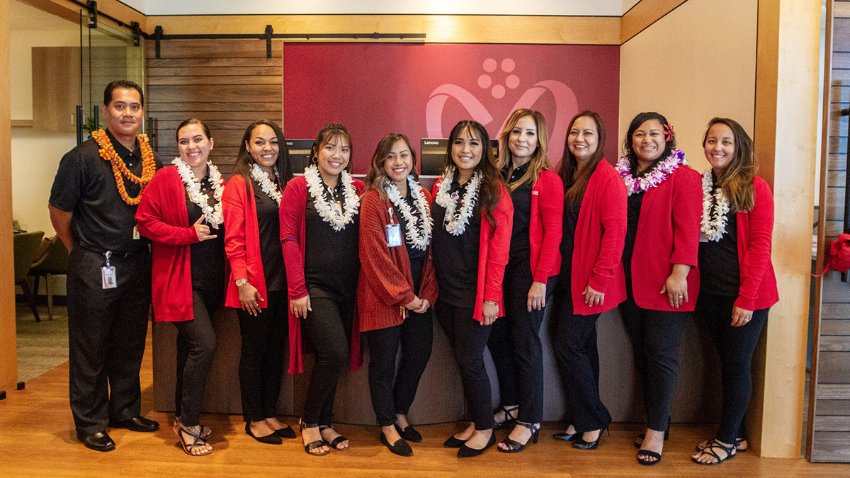 Group of 10 professionally dressed people wearing Hawaiian leis standing in a row in a building lobby.