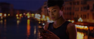Woman dressed formally standing outside looking at her phone with city lights glowing in the background