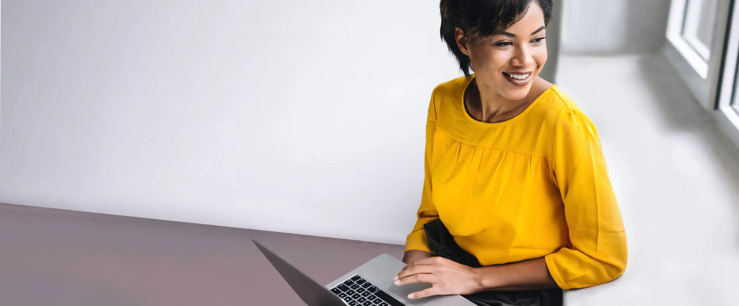 A young woman in yellow top working on a laptop with a smile