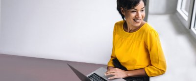 A young woman in yellow top working on a laptop with a smile