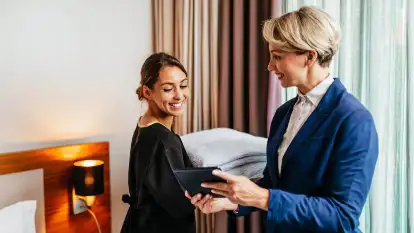 Housekeeping Supervisor checking on one of her Room Attendants as she makes the bed in the hotel room