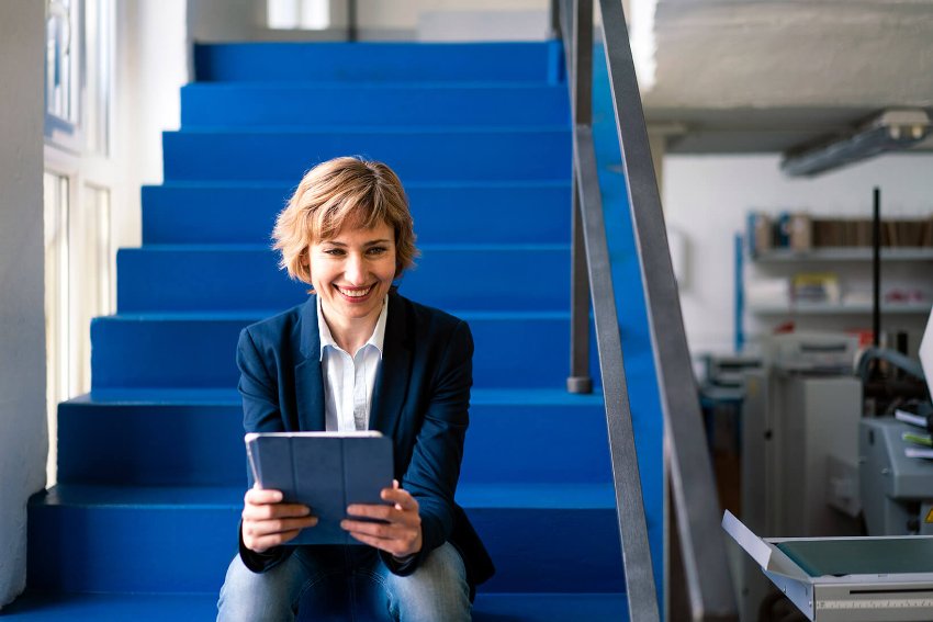 A well-dressed, suited woman sitting at a desk and working on her laptop