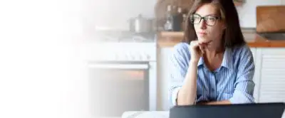 Woman sitting in front of a laptop in the kitchen looking pensive